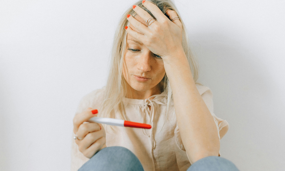 Femme inquiète tenant un test de grossesse, illustrant le tabou du premier trimestre et l’angoisse liée à la fausse couche.